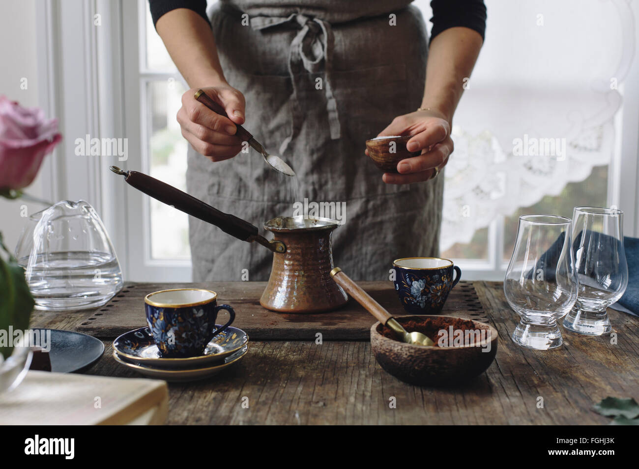 A woman is placing sugar in a small pot to make Turkish Coffee. Stock Photo