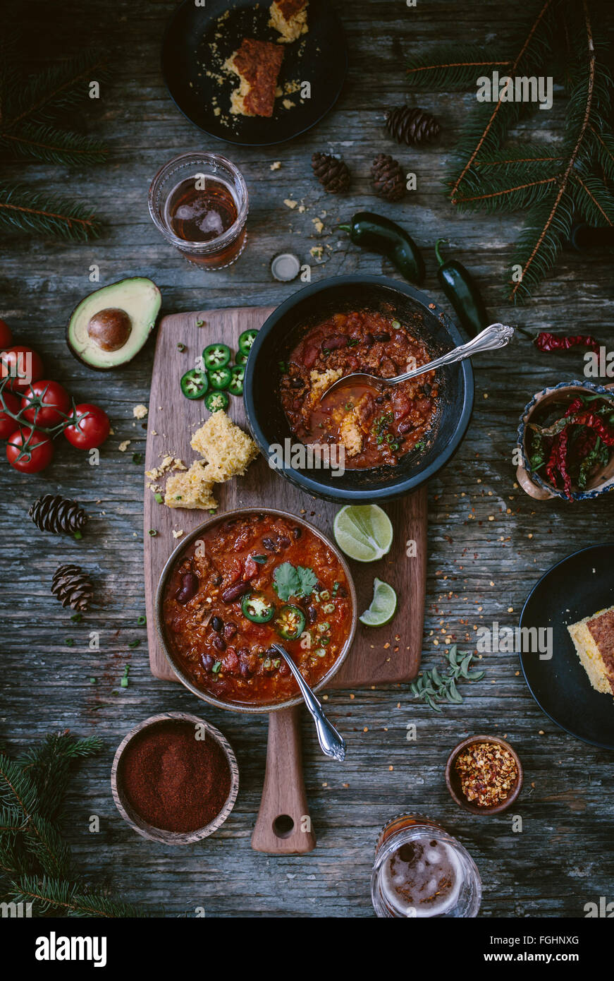 Two bowls of Turkey and Bean chili surrounded with two glasses of beer corn bread tomatoes chili powder and jalapenos on a v Stock Photo