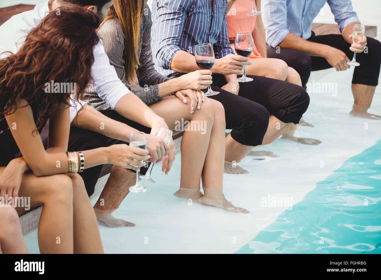 Young people sitting by swimming pool Stock Photo