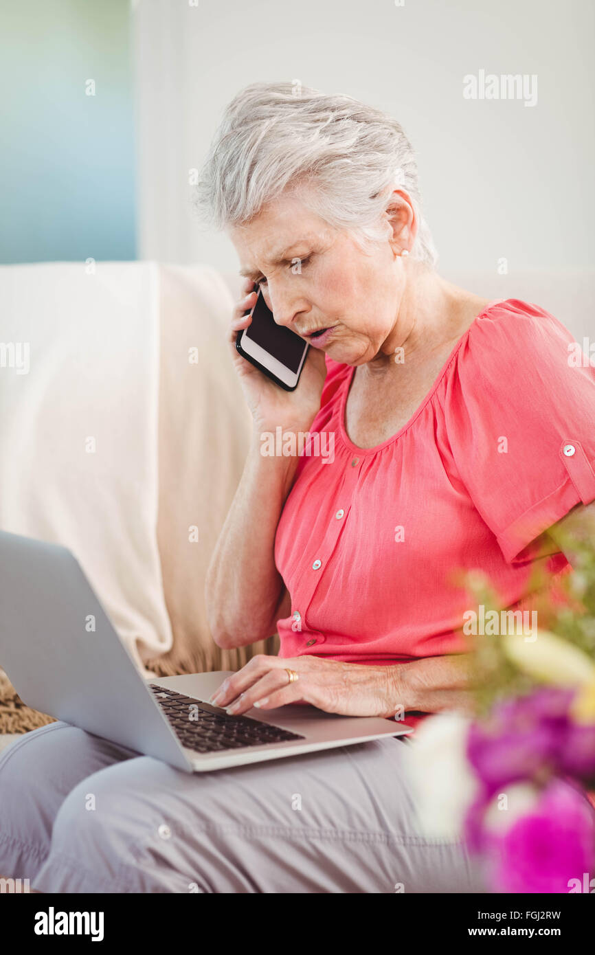 Senior woman talking on phone and using laptop Stock Photo - Alamy