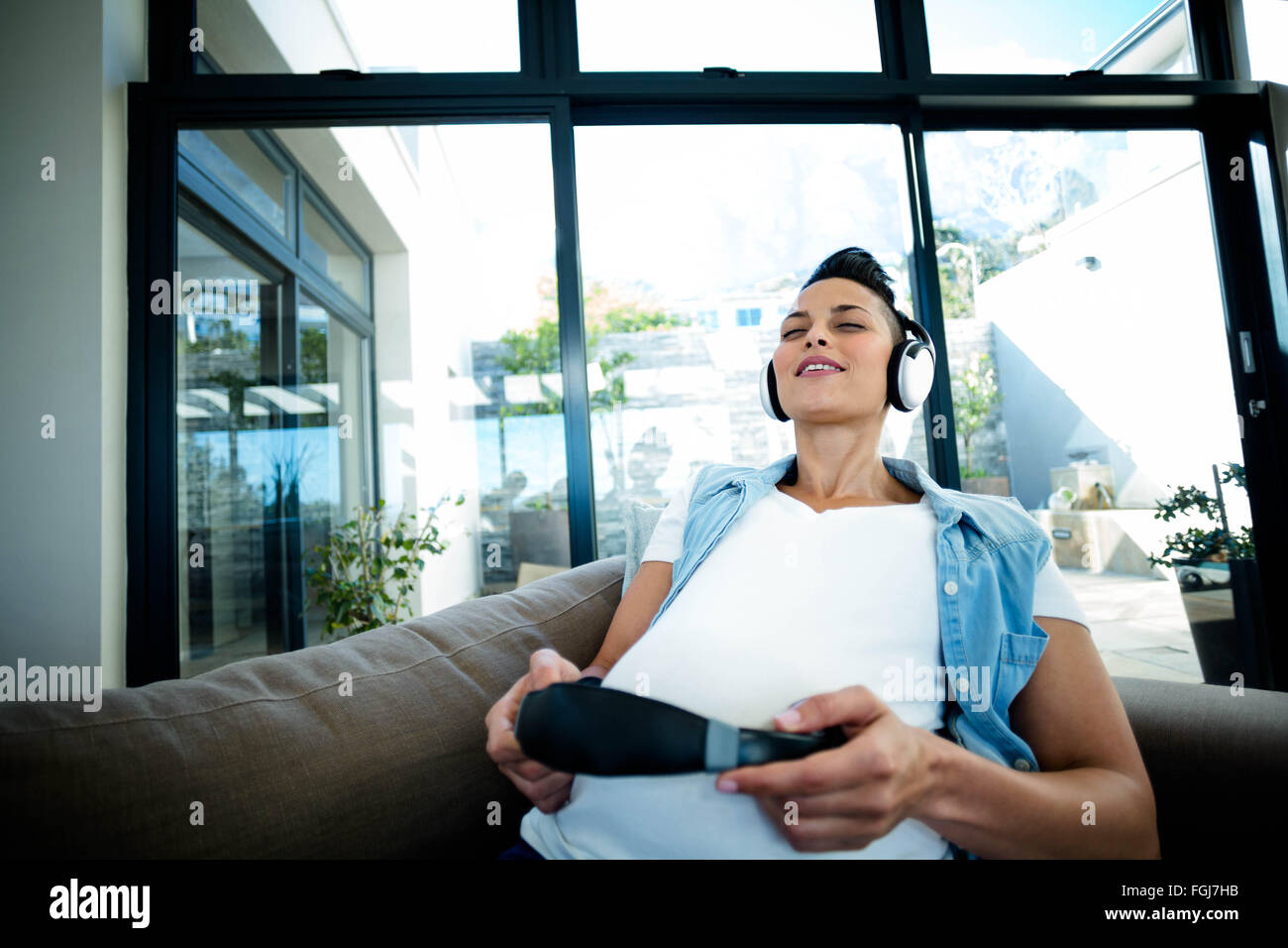 Pregnant woman listening to music on sofa Stock Photo - Alamy