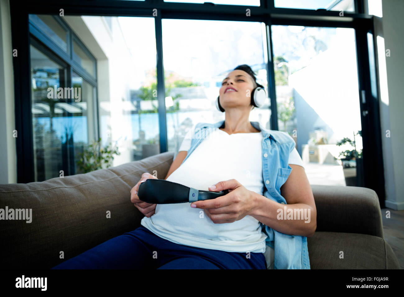 Pregnant woman listening to music on sofa Stock Photo - Alamy