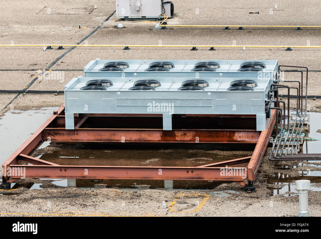 Ventilation fans, pipes, red steel bars, and other industrial machinery on flat roof top, in puddles of standing water. Stock Photo