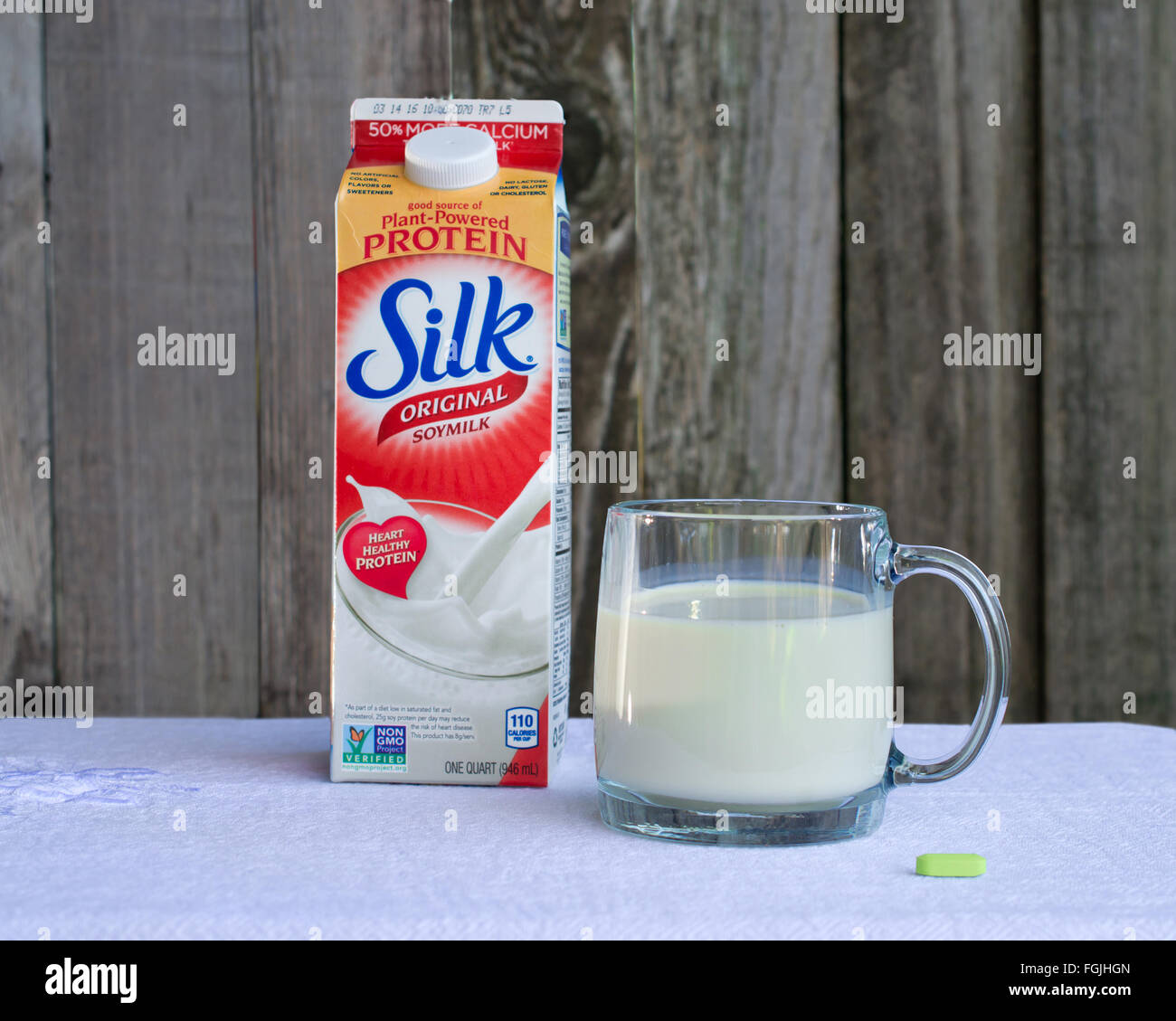 Silk soy milk with added calcium and an oyster-shell calcium pill on table, against wooden background Stock Photo