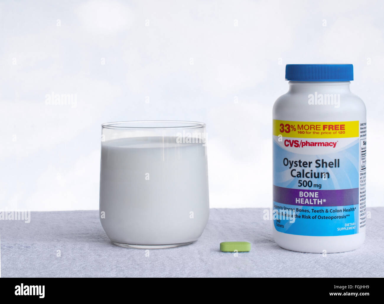 A pill and a bottle o of oyster shell calcium, and a cup of milk, on a table, against white background Stock Photo