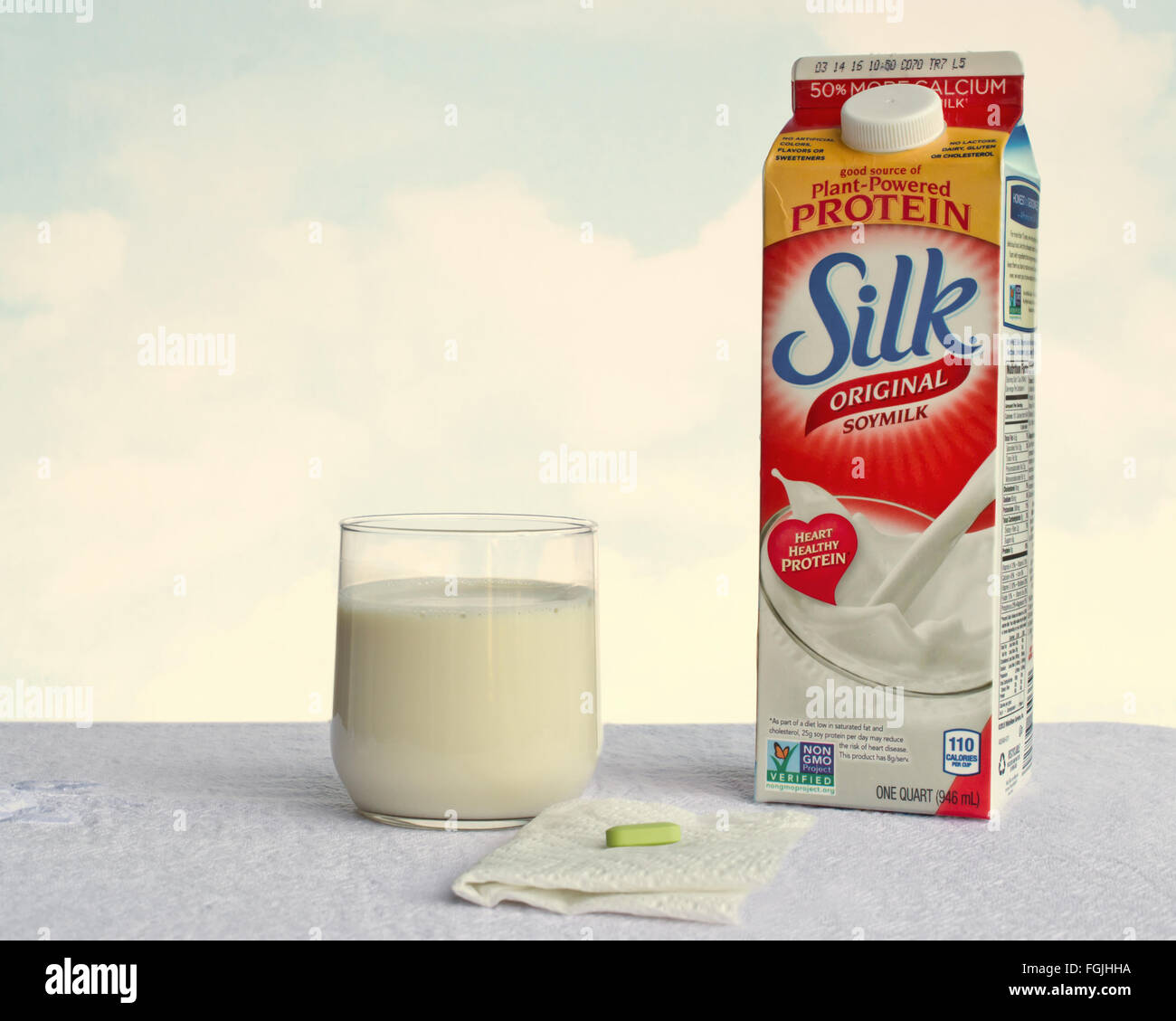 Silk soy milk with added calcium and an oyster-shell calcium pill on table, against clouds background Stock Photo