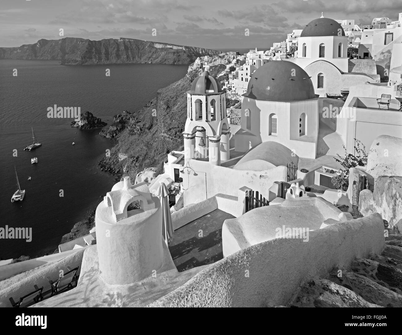 Santorini - The look to typically blue church cupolas in Oia over the caldera and the Therasia island in the background. Stock Photo