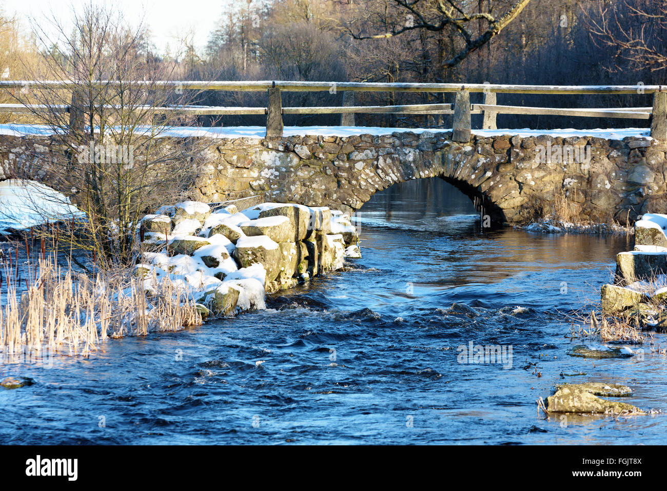 Detail of Blidingsholm stone arch bridge that crosses the river Morrumsan. Thin layer of snow cover the ground and stones. Small Stock Photo