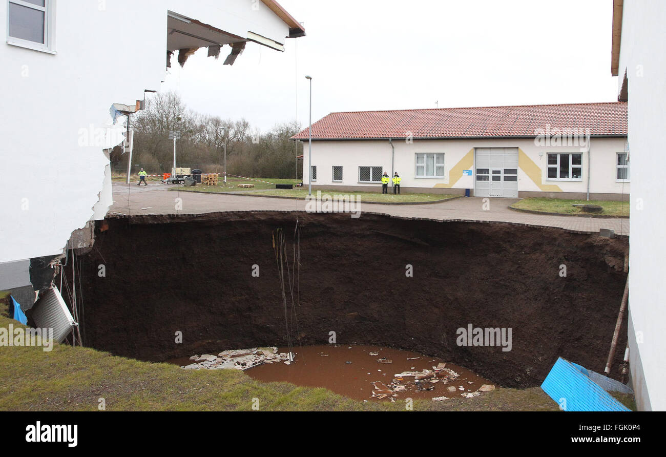Nordhausen, Germany. 20th Feb, 2016. General view of a sinkhole between two damaged buildings on the former compound of the civil protection agency (Katastrophenschutz) in Nordhausen, Germany, 20 February 2016. The sinkhole reportedly opened late 19 February evening between the two uninhabitated buildings and left a crater with a depth of some 50 metres. The hole has filled with water since then, nobody was hurt in the incident. Photo: SEBASTIAN WILLNOW/dpa/Alamy Live News Stock Photo