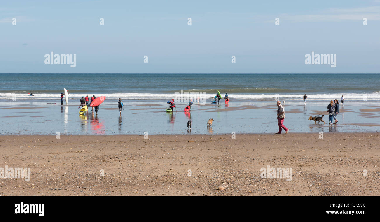 Seascape from shore showing holiday makers, waves and yachts with blue sky. Stock Photo