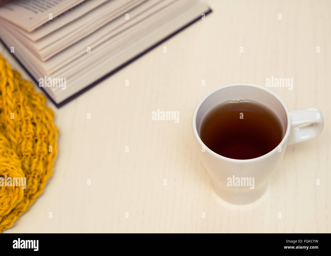 White cup of tea, book and scarf on light wooden desk. Selective focus, toned Stock Photo