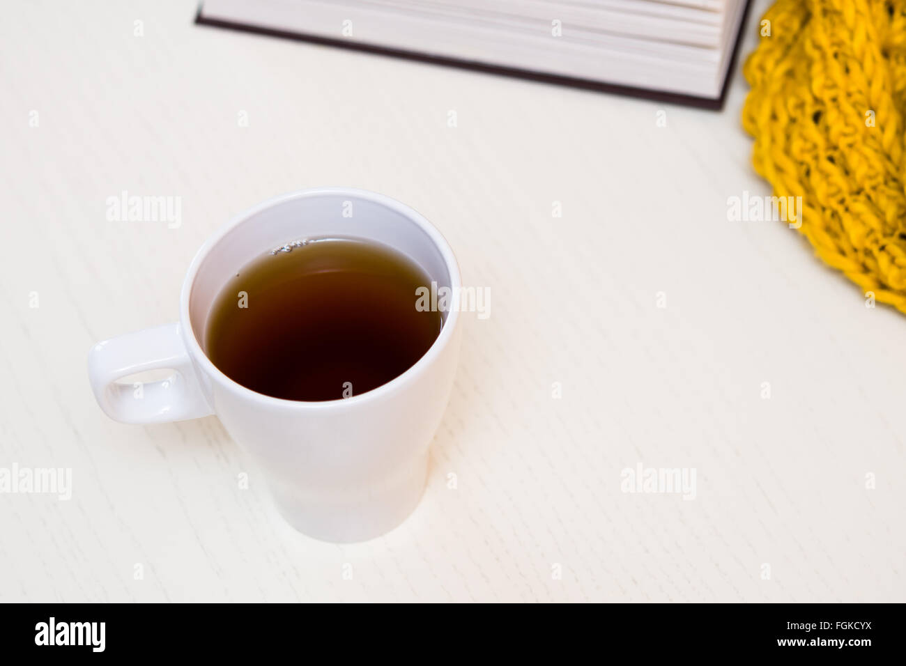 White cup of tea, book and scarf on light wooden desk. Selective focus, toned Stock Photo