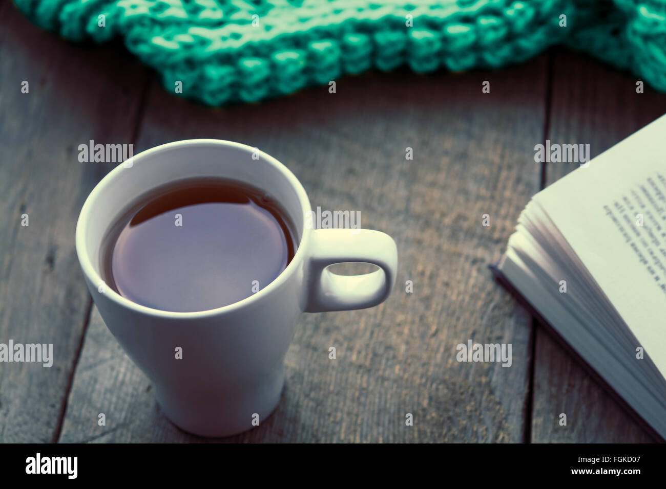 White cup of tea, book and scarf on old wooden desk. Selective focus, toned Stock Photo