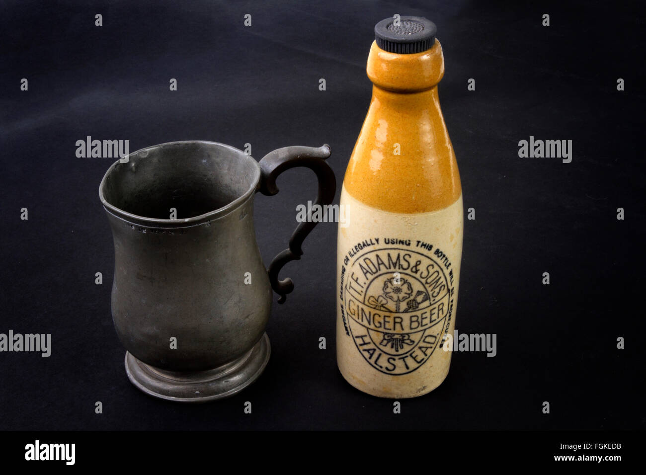 Antique stoneware ginger beer bottle and a George IV pewter one pint beer mug on a black background Stock Photo