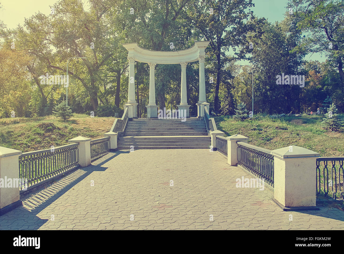 Old Greek style columns in Park. Antique style architecture. Retro toned image. Solar flare. Stock Photo