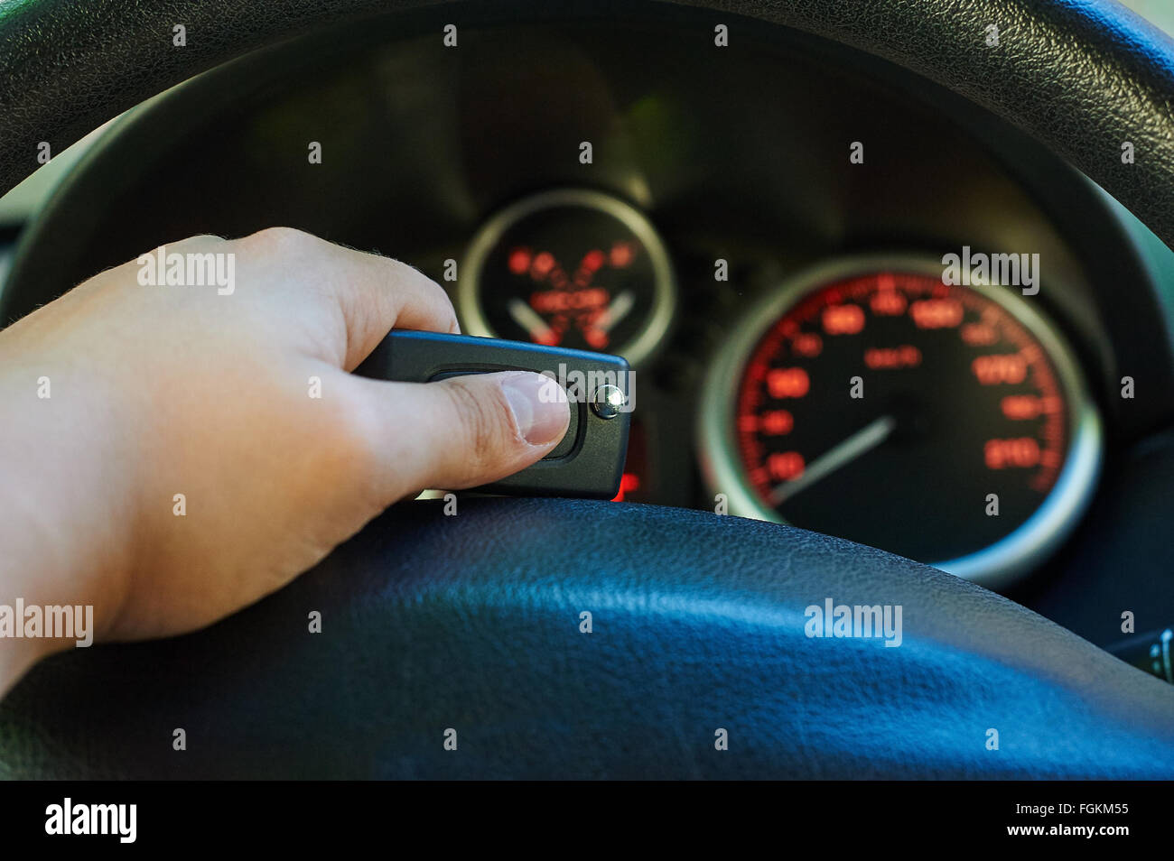 Man driver hand holding car key. Orange glowing meters with a red needle. Fuel, tachometer, odometer and speedometer. Stock Photo