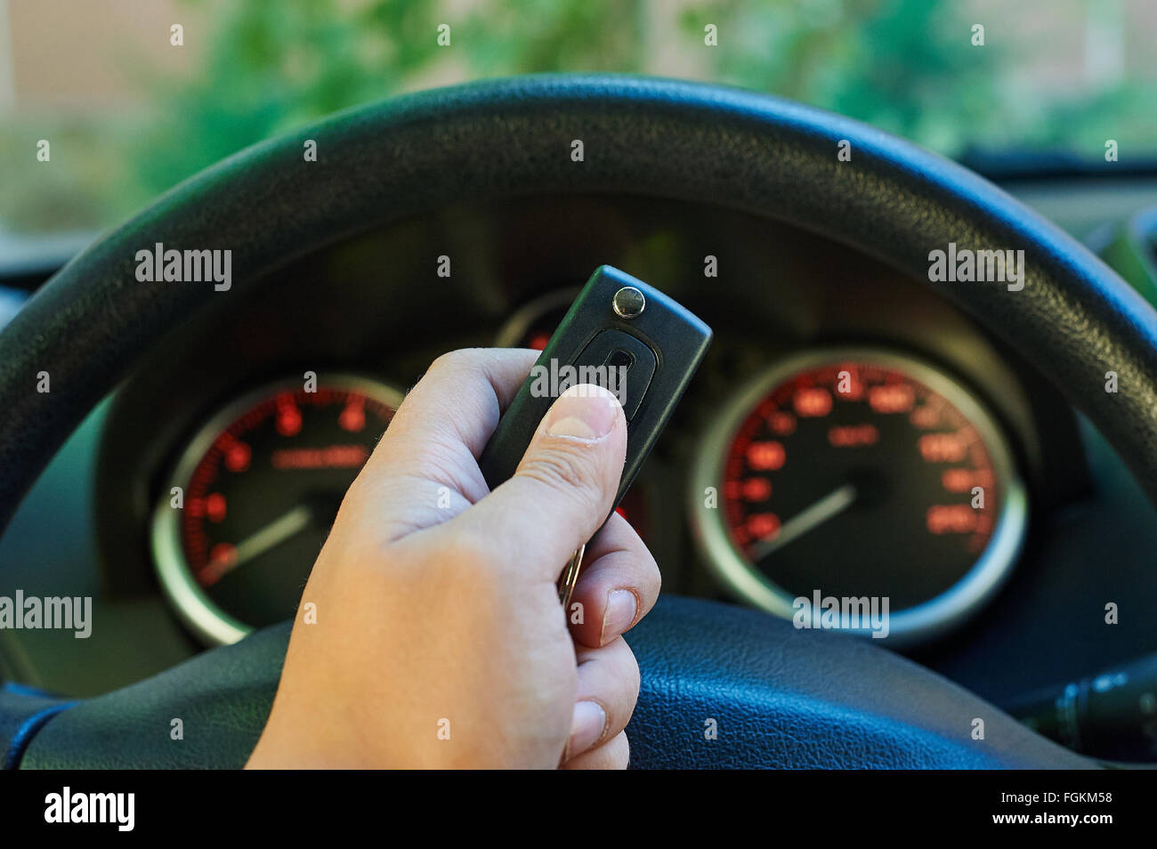 Man driver hand holding car key. Backlit gauges of an automobile. Orange glowing meters with a red needle. Fuel, tachometer, odo Stock Photo