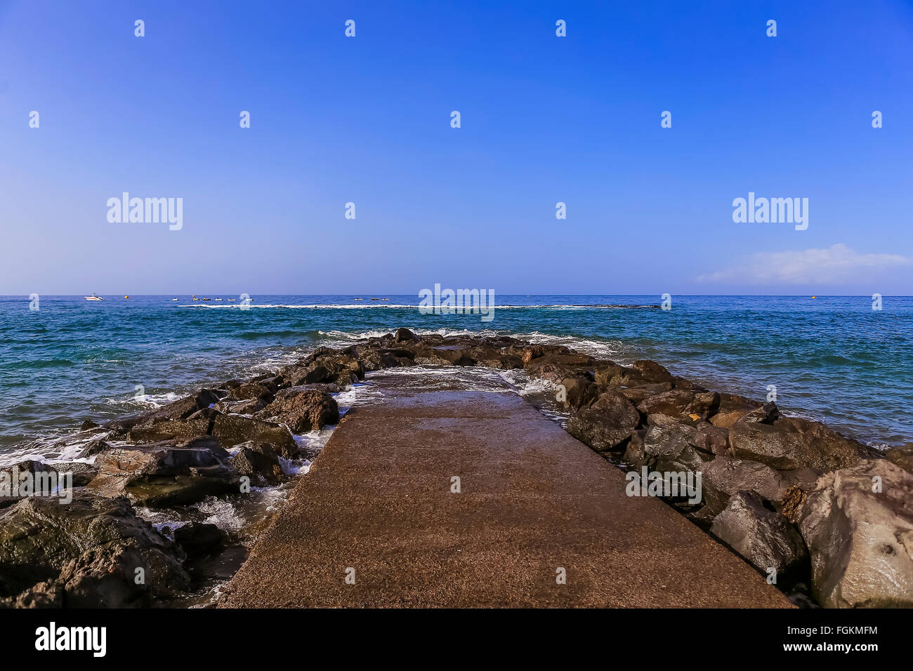 Sea breakwater amid calm waters and blue sky Stock Photo