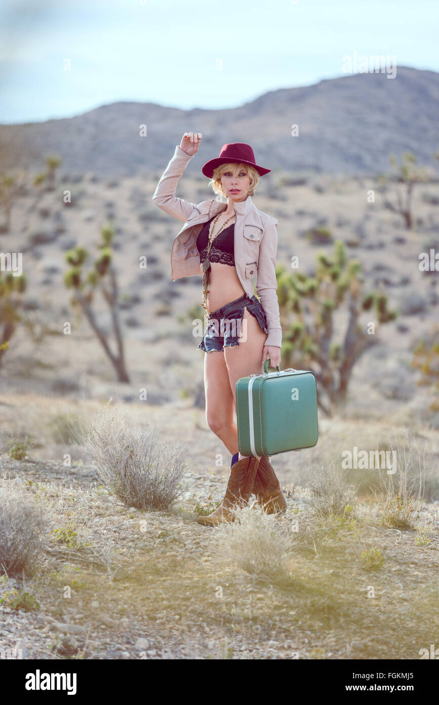 fashionable woman traveler walking with suitcase and luggage in desert Stock Photo