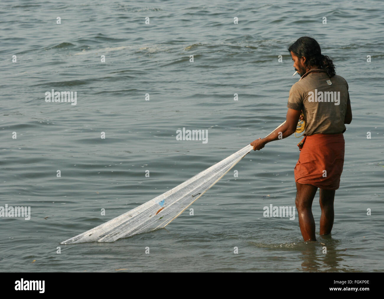 a young Indian fisherman smoking in a lungi hawling pulling in his fishing net from the beach, India Stock Photo