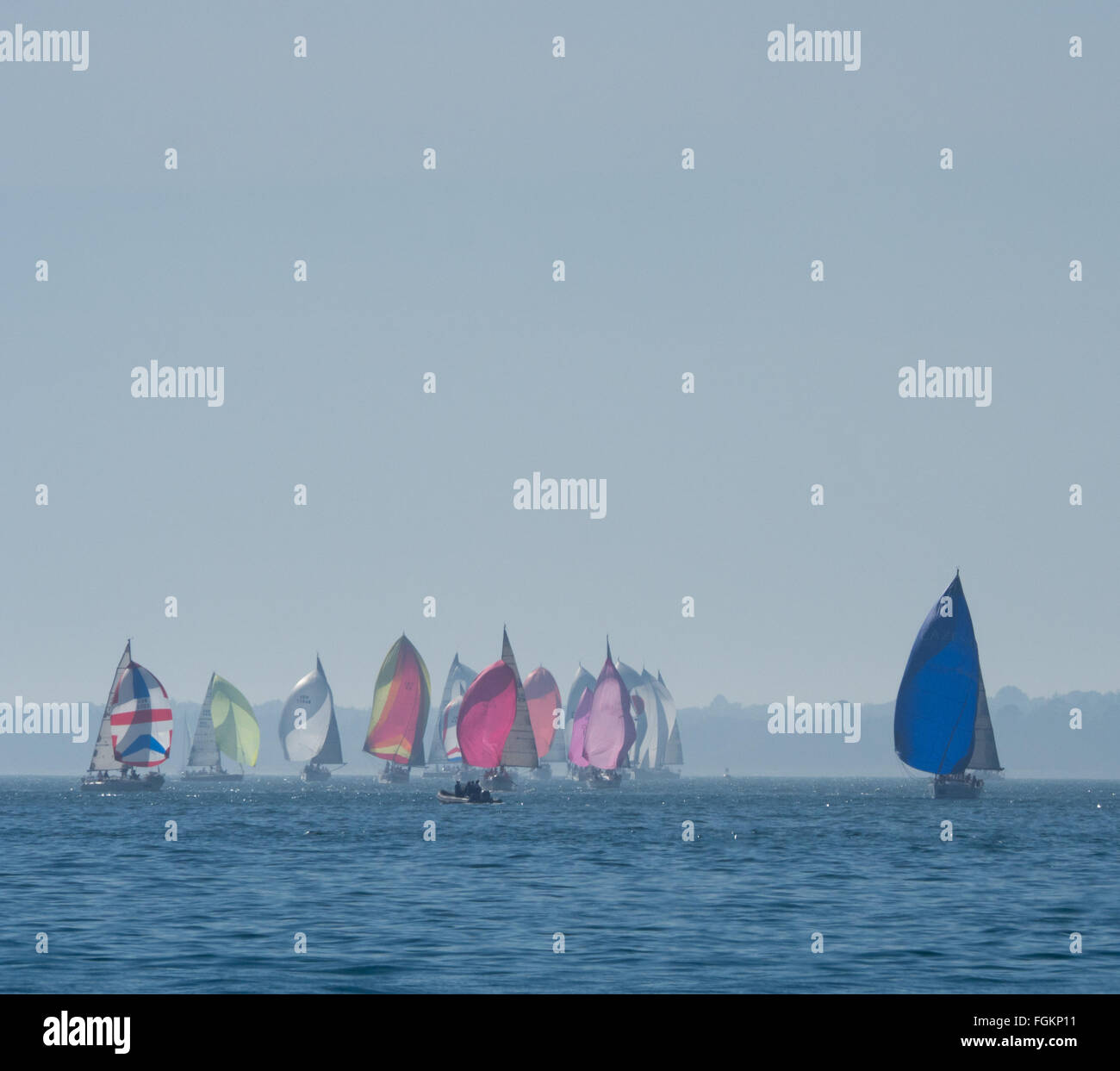 a group of yachts racing with full colorful colourful spinnakers on calm water under a large clear blue Solent sky, Cowes Week, UK Stock Photo