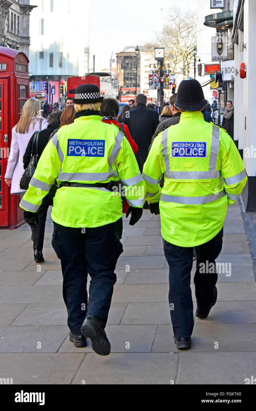 Metropolitan Police back view female officer in distinctive cap left & male officer traditional helmet patrolling West End London England UK Stock Photo