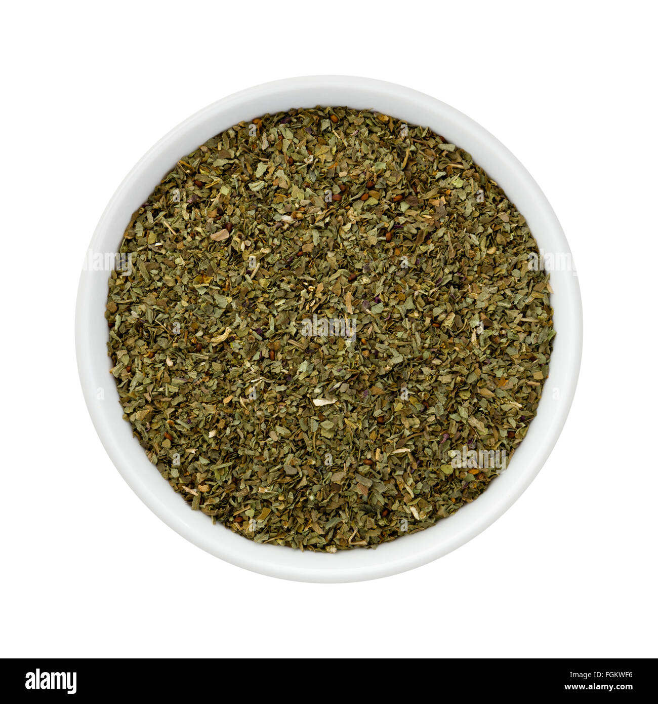 Dried Basil Flakes in a Ceramic Bowl. The image is a cut out, isolated on a white background. Stock Photo