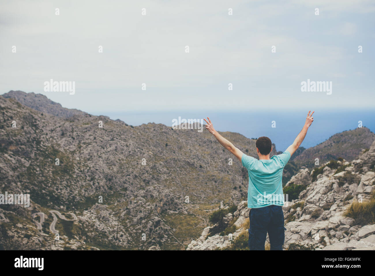 Young man standing on cliff with hands raised Stock Photo