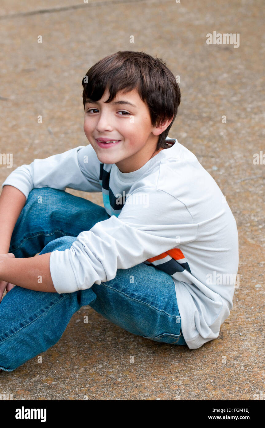 Portrait of a happy cute boy in denim jeans sitting on sidewalk Stock ...