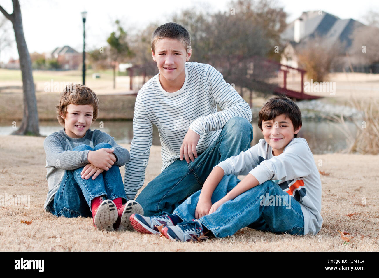 Group of three boys that are family and friends sitting on grass smiling. Stock Photo