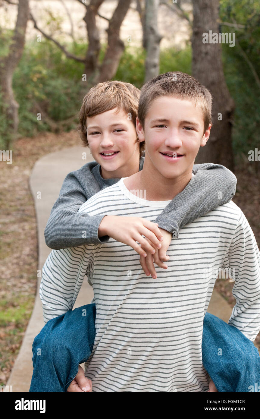 Two cute boys that are brothers riding piggy back on sidewalk smiling at camera. Stock Photo