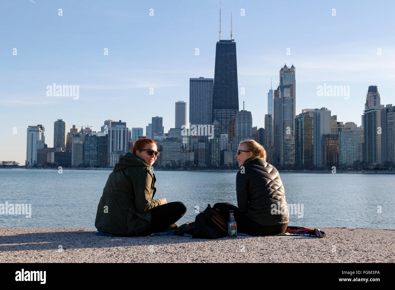 Chicago, USA 20th February 2016. Two young women enjoy the day sitting on the seawall at North Avenue Beach. Chicagoans and visitors alike came to the city's lakeshore to enjoy an unseasonably warm day with temperatures over 60ºF/15ºC. The high winds that blasted the city yesterday subsided to a gentle breeze. Credit:  Todd Bannor/Alamy Live News Stock Photo