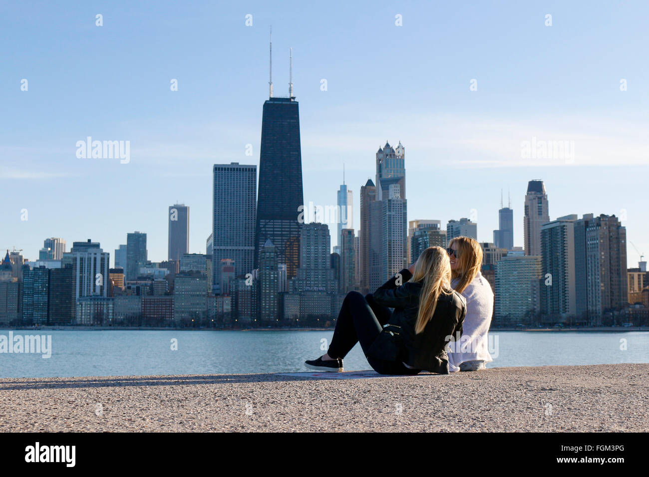 Chicago, USA 20th February 2016. Two young women sit on the seawall at North Avenue Beach. Chicagoans and visitors alike came to the city's lakeshore to enjoy an unseasonably warm day with temperatures over 60ºF/15ºC. The high winds that blasted the city yesterday subsided to a gentle breeze. Credit:  Todd Bannor/Alamy Live News Stock Photo