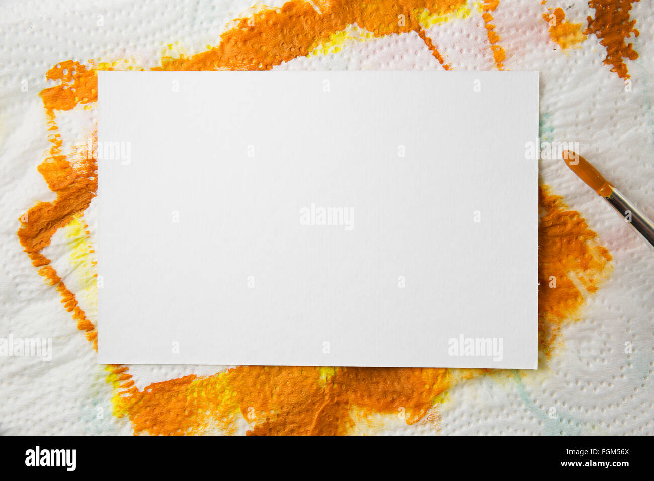 Blank white watercolor paper on towel with orange paint and paintbursh covered with orange paint. Stock Photo