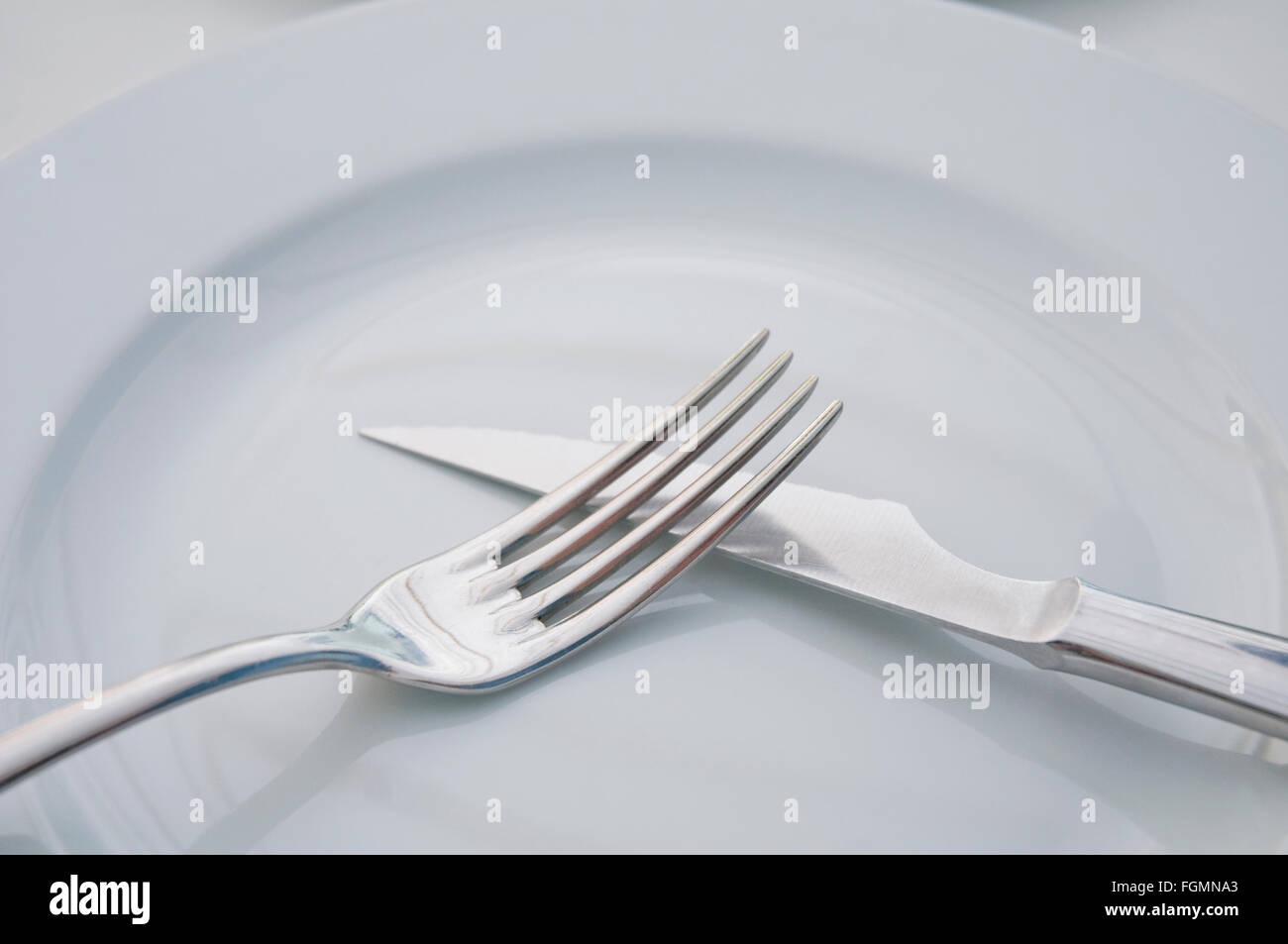 Fork and knife crossed on an empty dish. Close view. Stock Photo