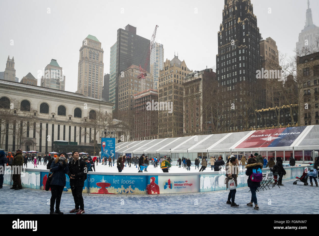 People enjoying the free outdoors ice rink in the snow at the Bank of America Winter Village in Bryant Park, New York Stock Photo