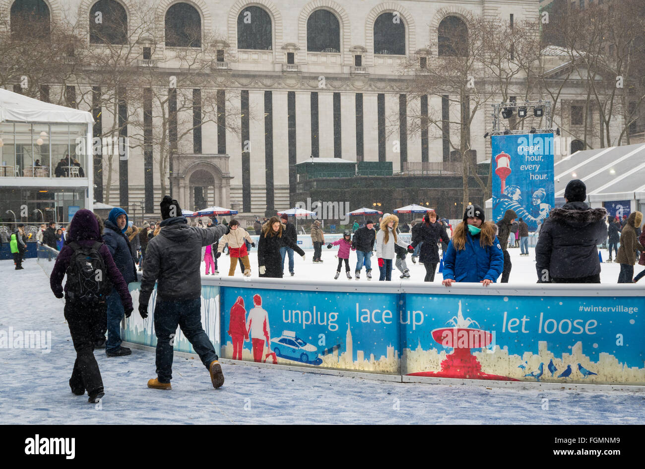 People enjoying the free outdoors ice rink in the snow at the Bank of America Winter Village in Bryant Park, New York Stock Photo