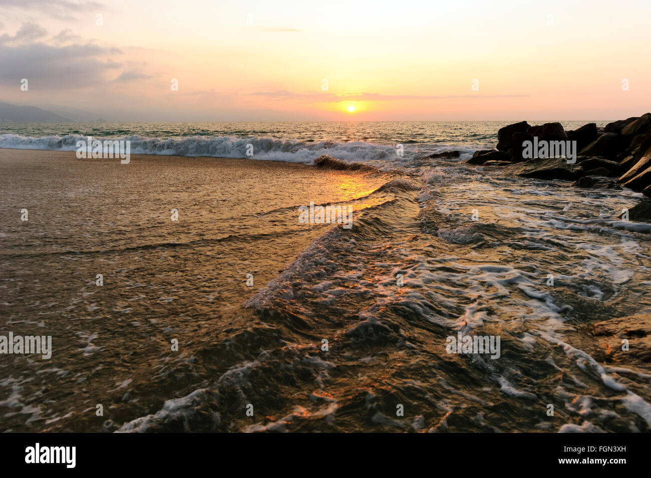 Seascape sunset is a sunset on the beach with large rocks in the foreground and a warm setting sunset sky on the ocean horizon. Stock Photo