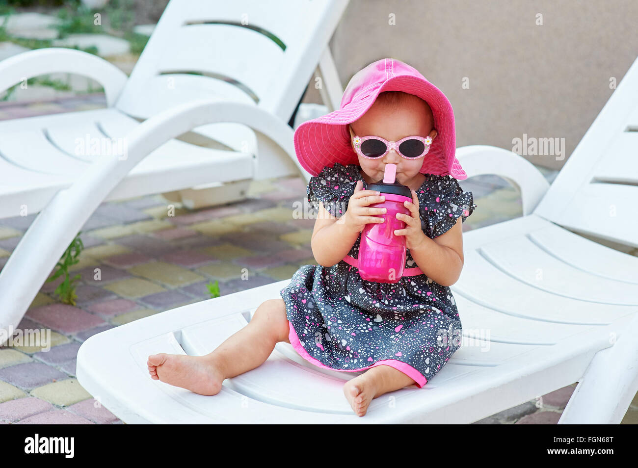 Little baby girl in autumn park drinks from pink plastic bottle Stock Photo