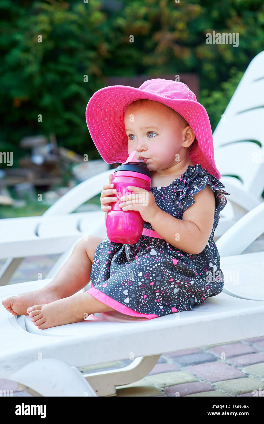 Little baby girl in autumn park drinks from pink plastic bottle Stock Photo