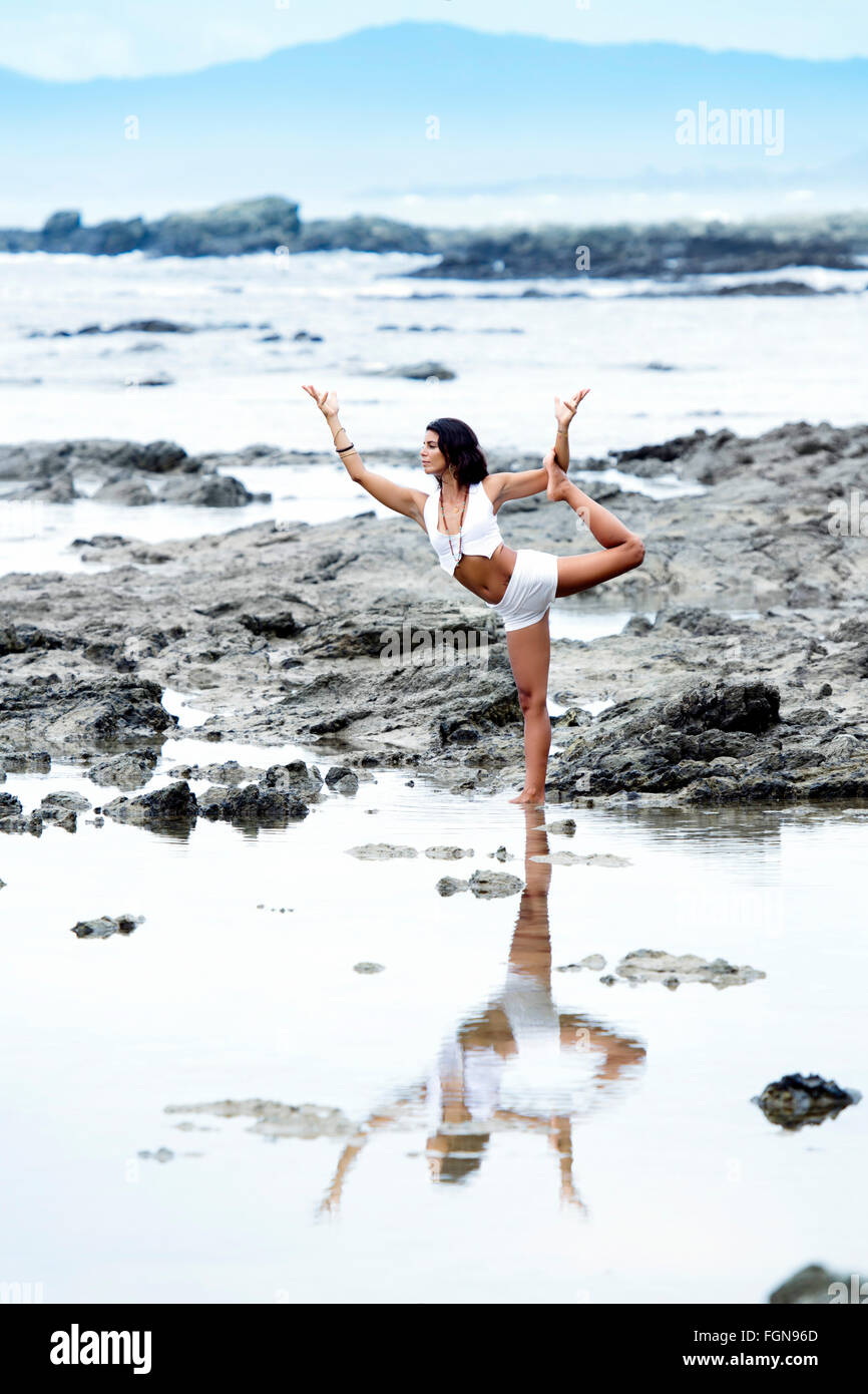 A young Latin woman in white practising yoga on the beach in Santa Teresa - a location famous for its wellness, Nicoya Peninsula, Costa Rica Stock Photo