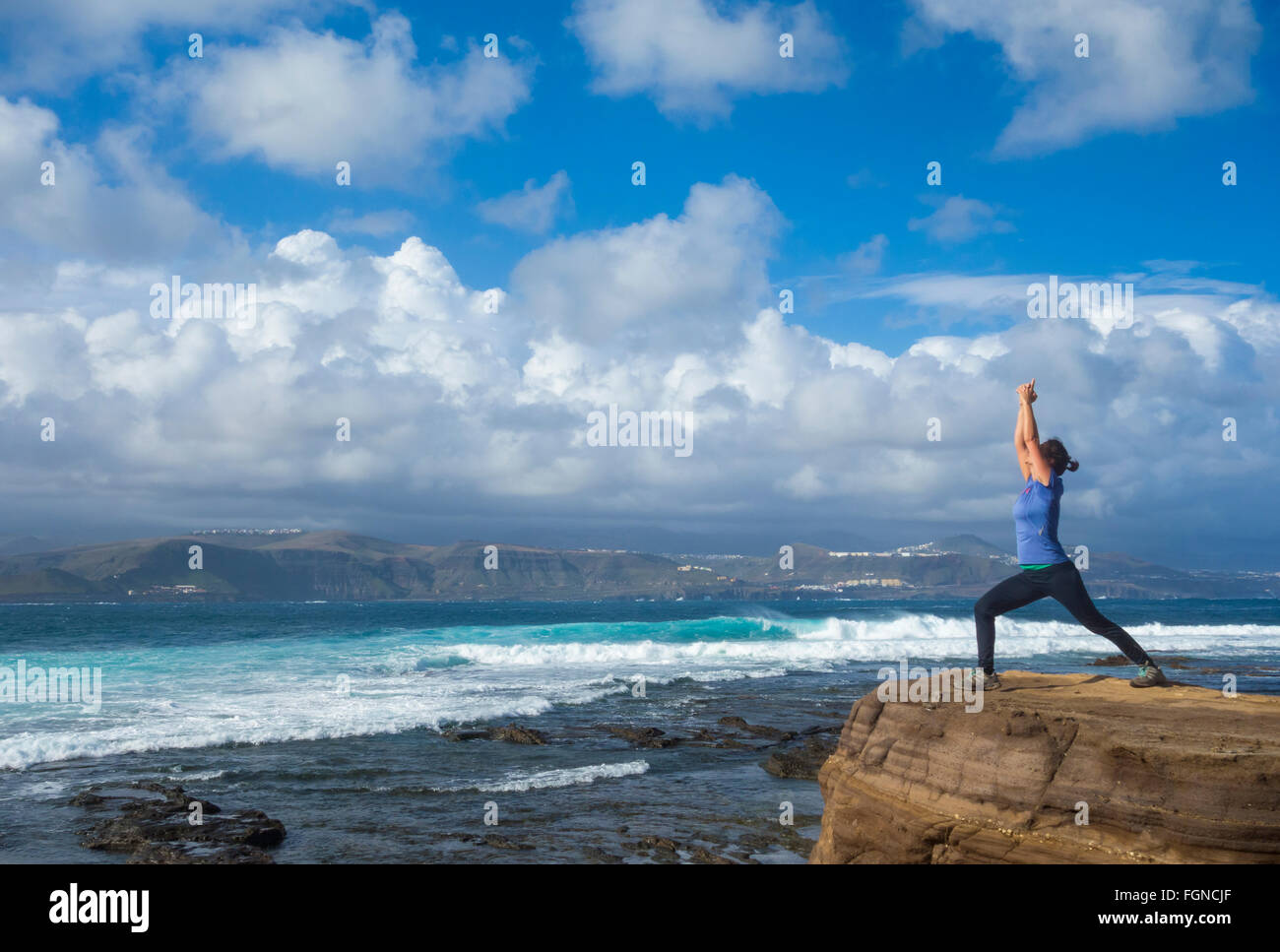 Mature female jogger warming up with Yoga stretching exercises on rock overlooking the sea. Stock Photo