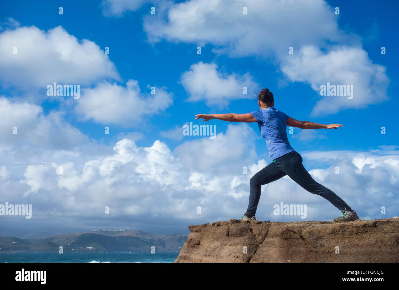 Mature female jogger warming up with Yoga stretching exercises on rock overlooking the sea. Stock Photo