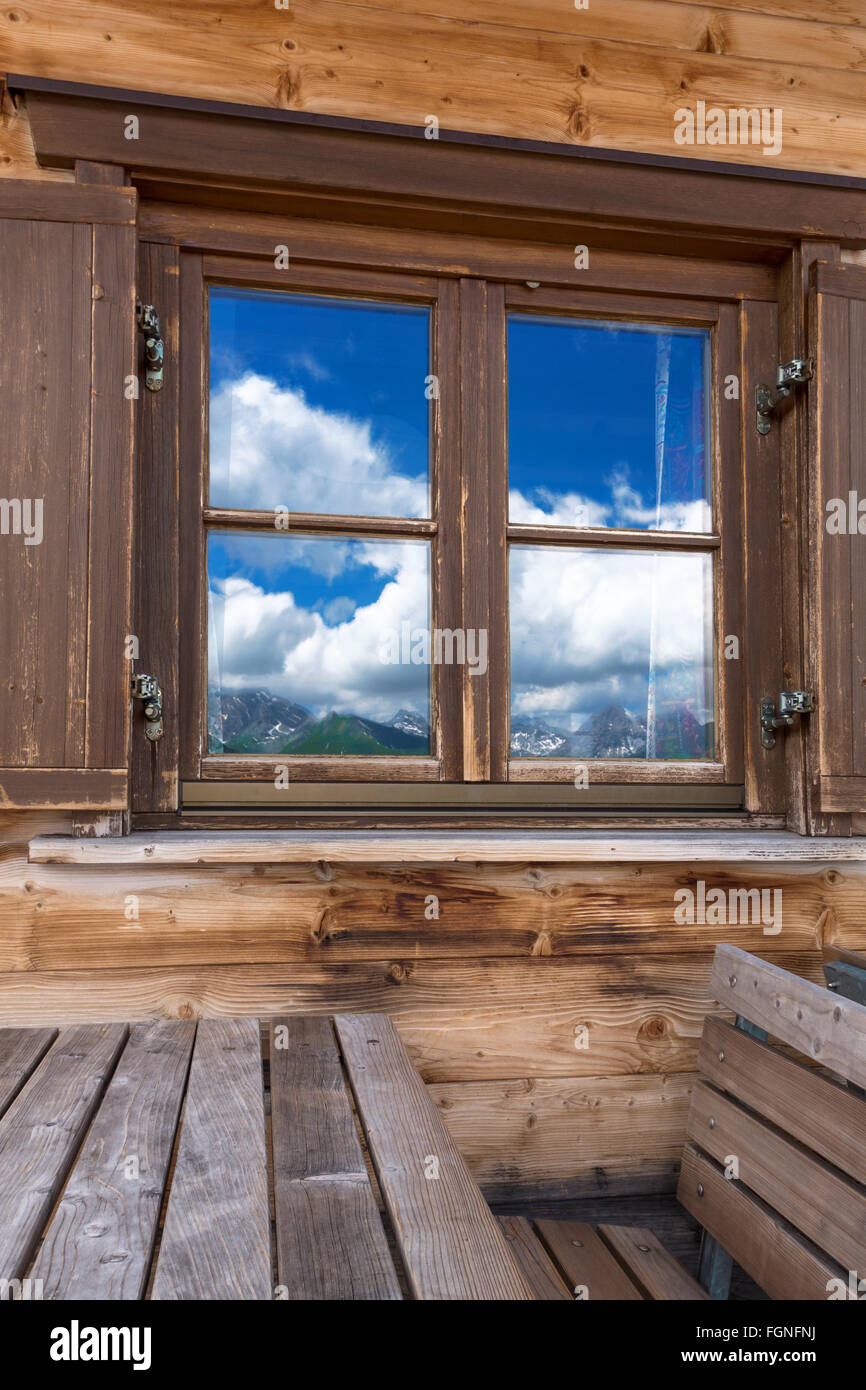Mountain landscape is reflected in the window of a rustic wooden ...