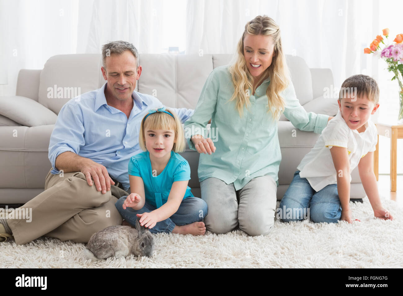 Smiling family with their rabbit on the rug Stock Photo - Alamy