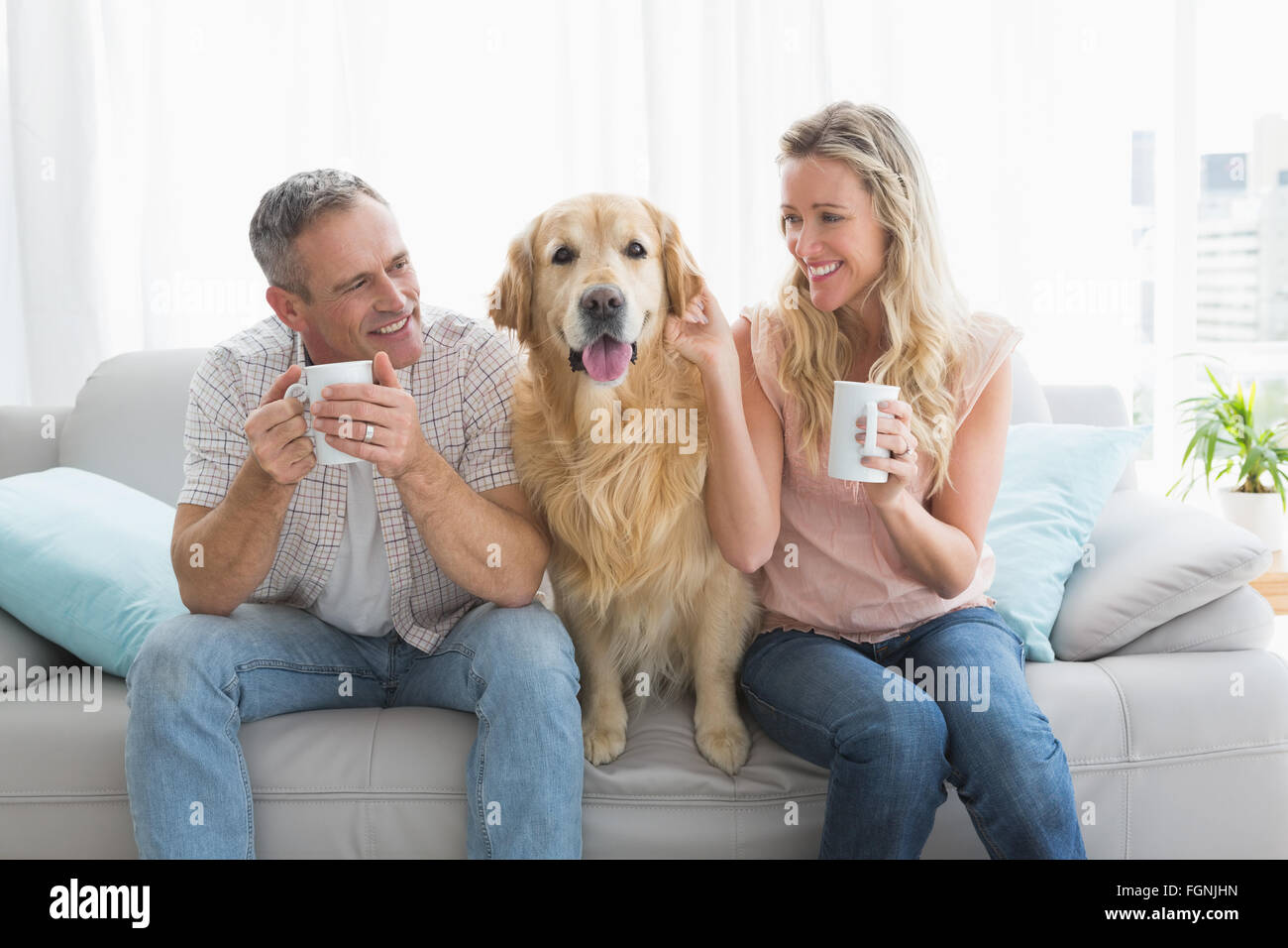 Smiling casual couple sitting on couch having coffee Stock Photo - Alamy