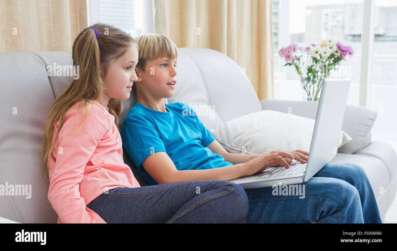 Happy siblings using laptop on sofa Stock Photo - Alamy