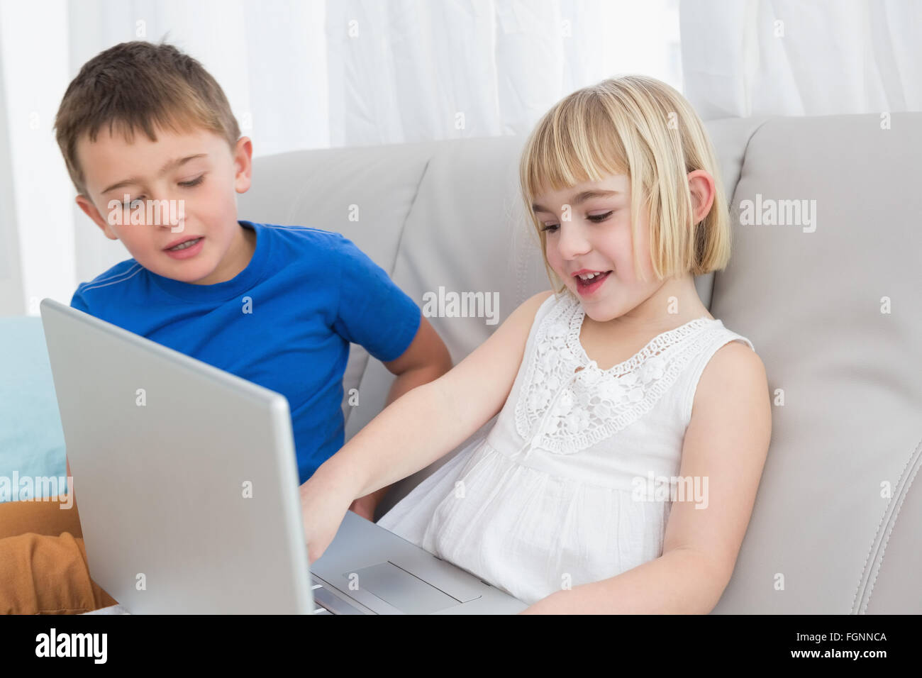 Siblings sitting on the couch using laptop Stock Photo - Alamy