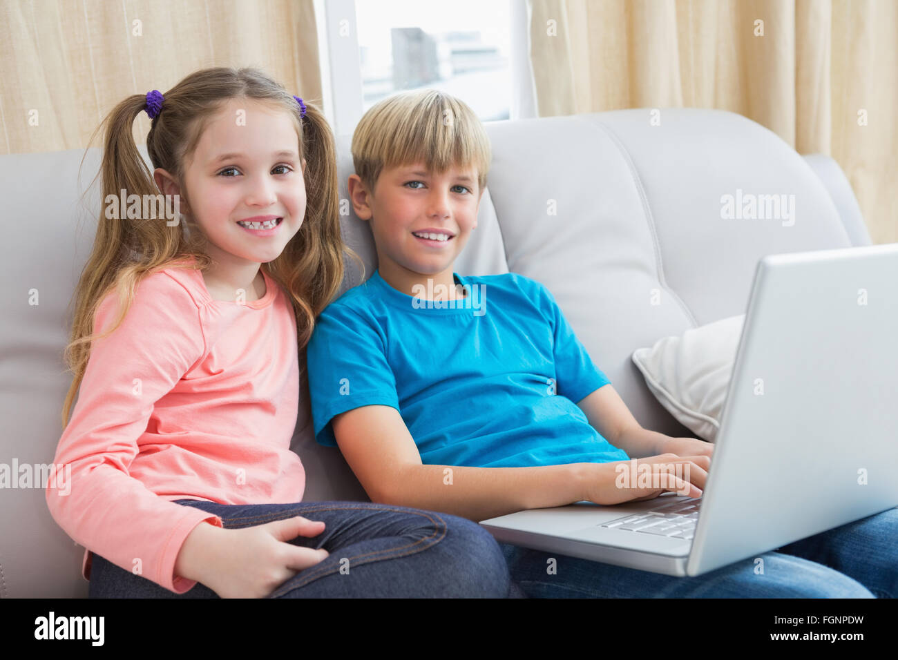 Happy siblings using laptop on sofa Stock Photo - Alamy