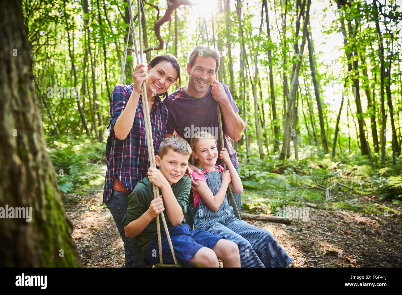 Portrait smiling family at rope swing in woods Stock Photo